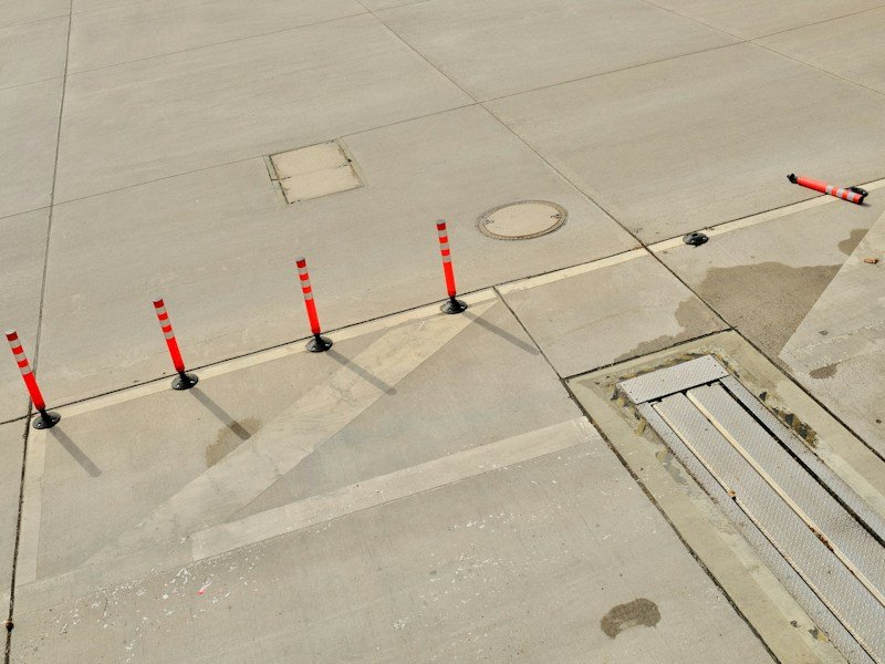 Cross-section diagram of a slab-anchored planter base plate showing wedge anchor, sealant detail, and wind force arrows