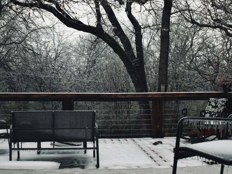 Insulated balcony planters wrapped in foam sleeves with straw mulch on a high-rise deck in winter
