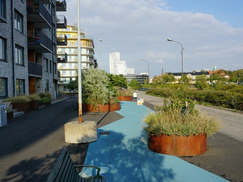 Stainless steel planter tie-down system anchoring a large pot on a high-rise balcony with glass railing
